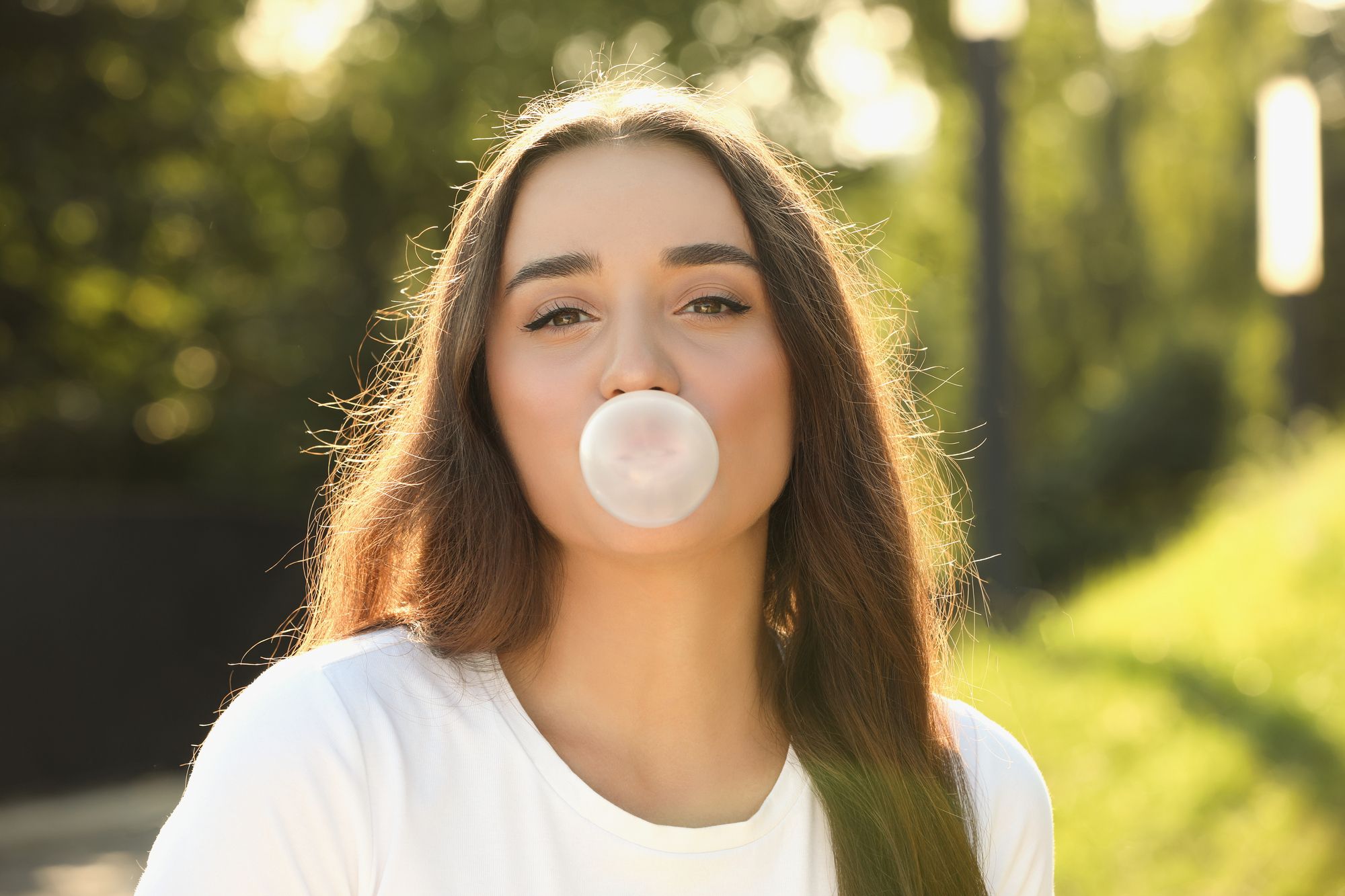 young woman with long brown hair blowing a bubble with gum