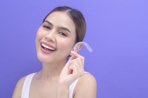woman holding Invisalign clear aligners on purple background
