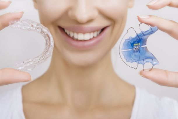 woman holding up clear aligner and retainer