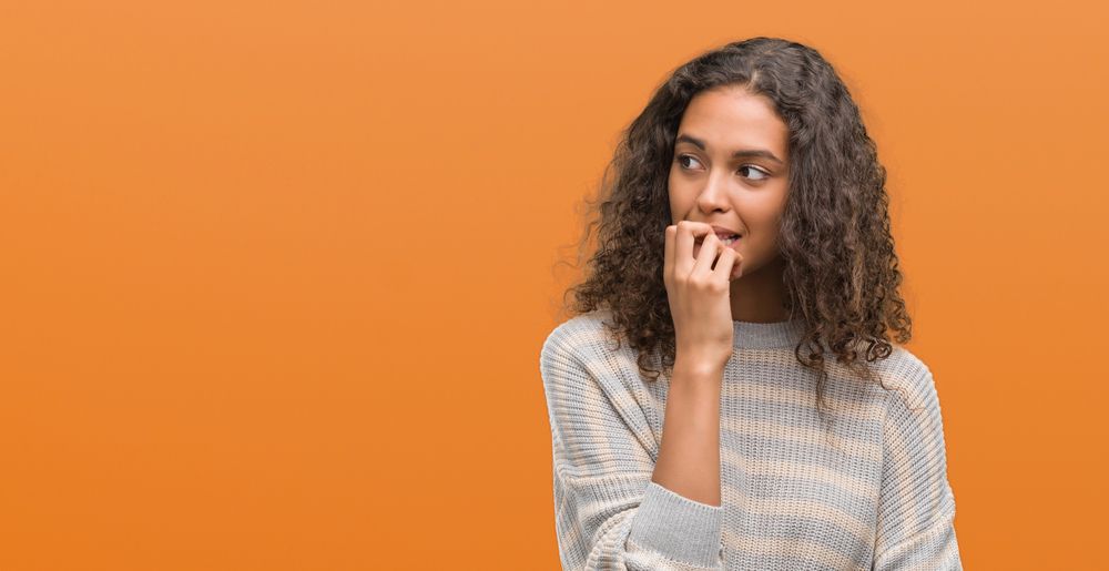 woman dealing with the Embarrassing Effects of Wearing Clear Aligners, covering her mouth, on orange background