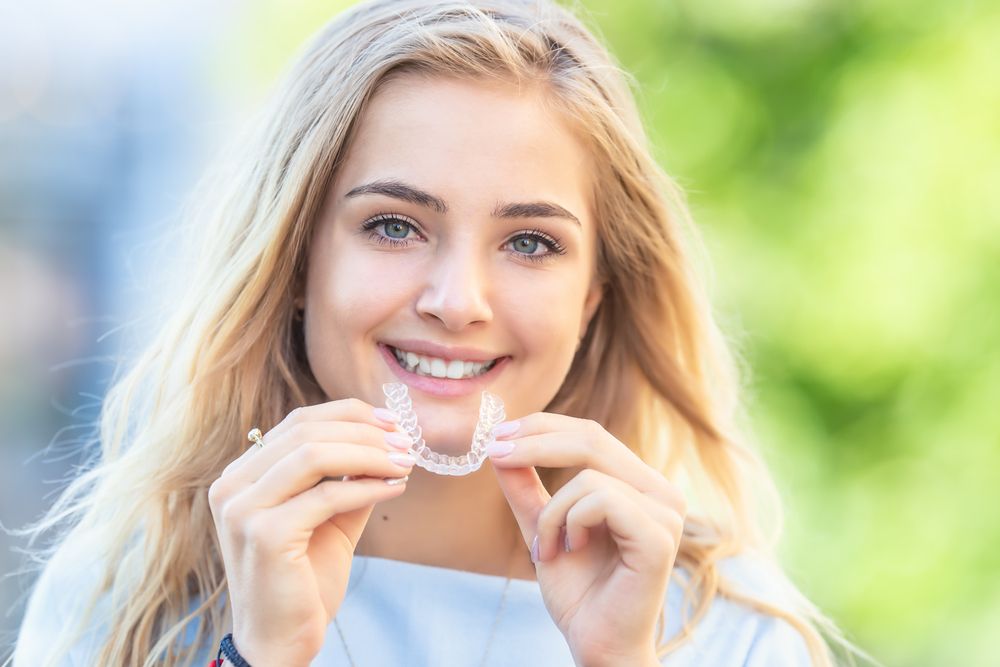 blonde teenager holding invisalign clear aligners