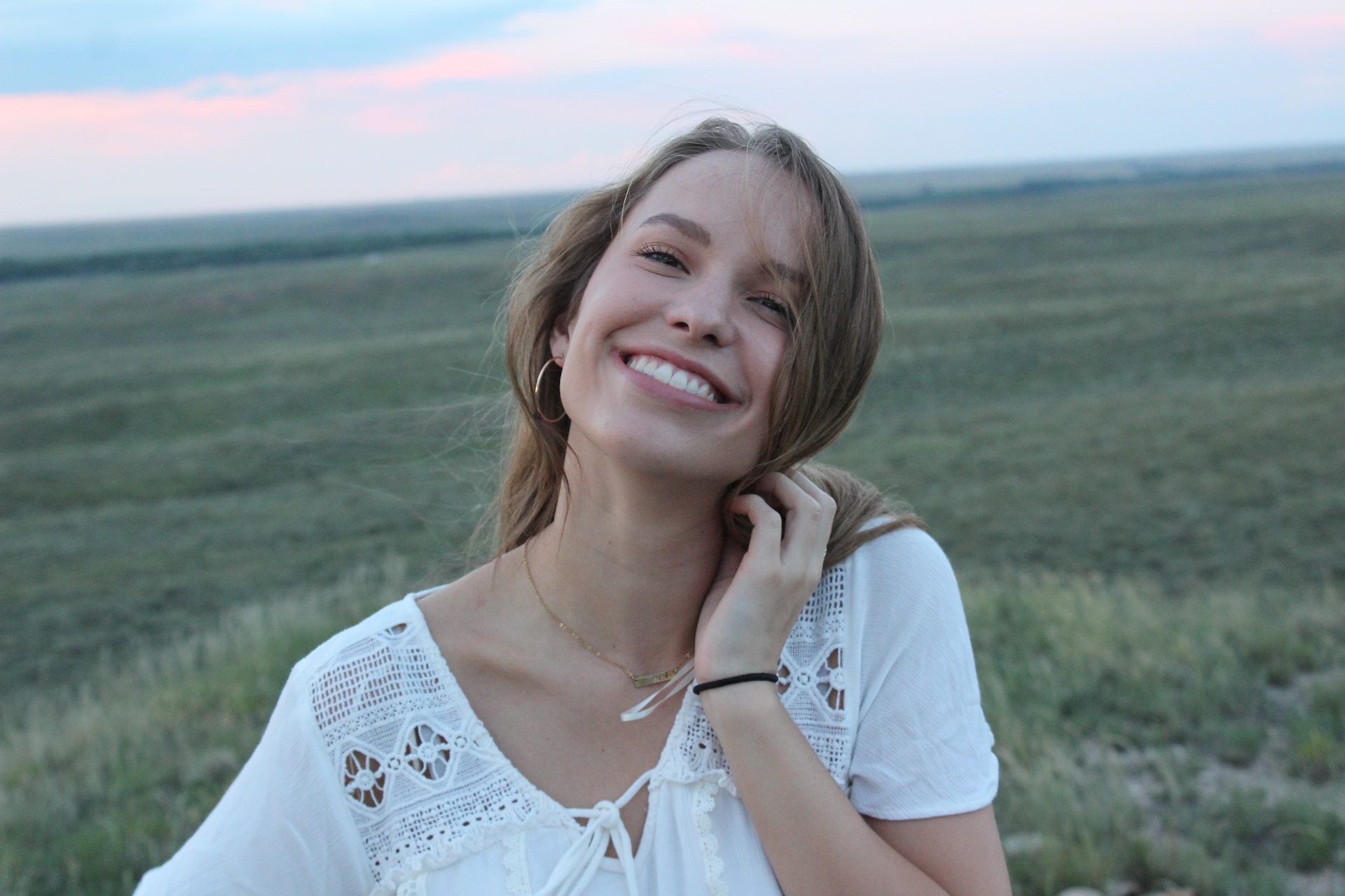 young woman smiling in a field wearing a white dress