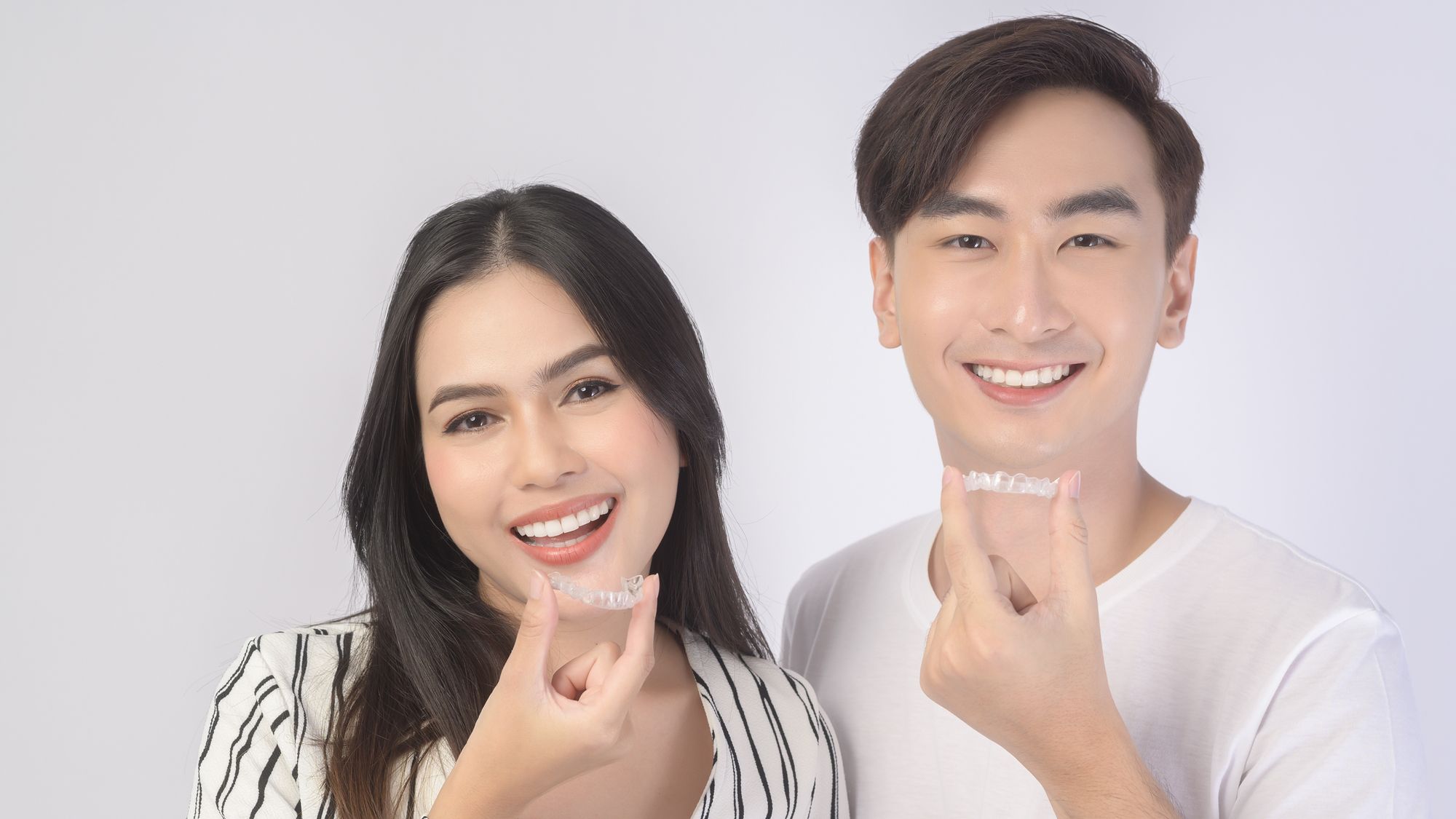 Young smiling man amd woman holding invisalign braces over white background studio, cosmetic dentistry and Orthodontic concept.