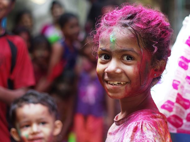 little indian girl covered in pink paint smiling at the camera