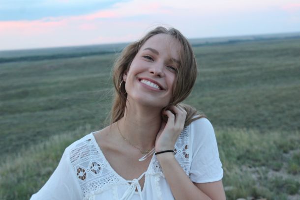 young woman smiling in a field wearing a white dress