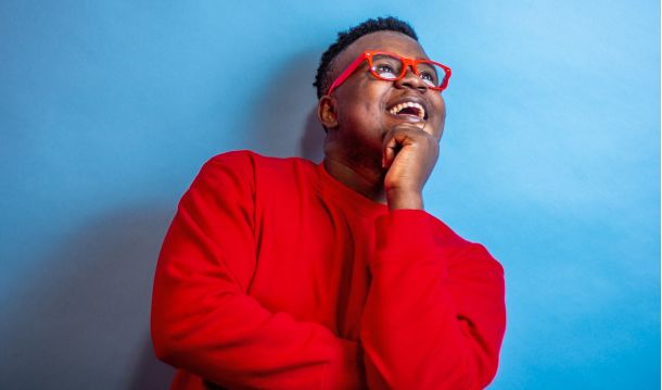 black man wearing a red jacket and glasses smiling on blue background